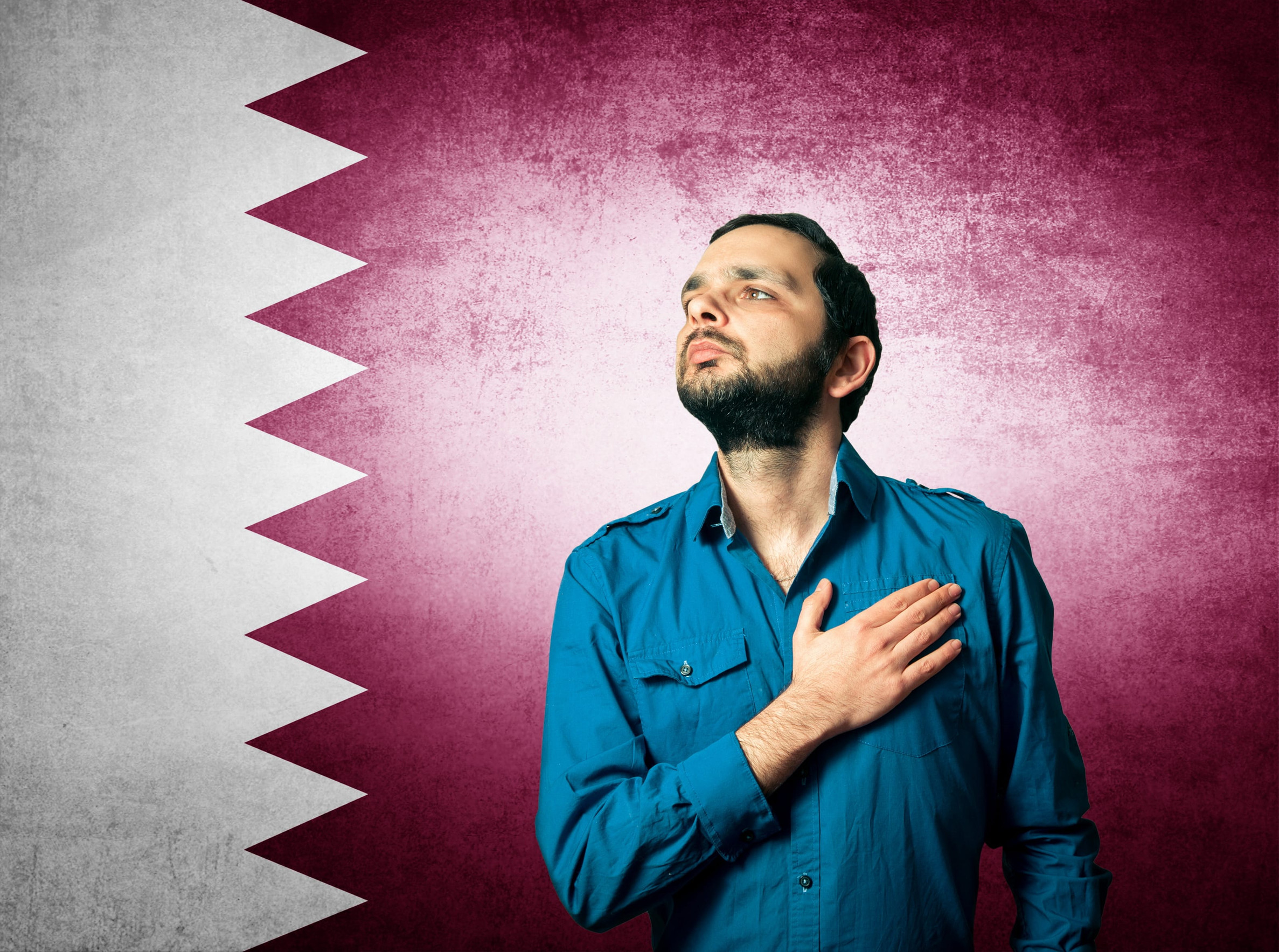 A patriotic man standing with a Qatar flag in the background